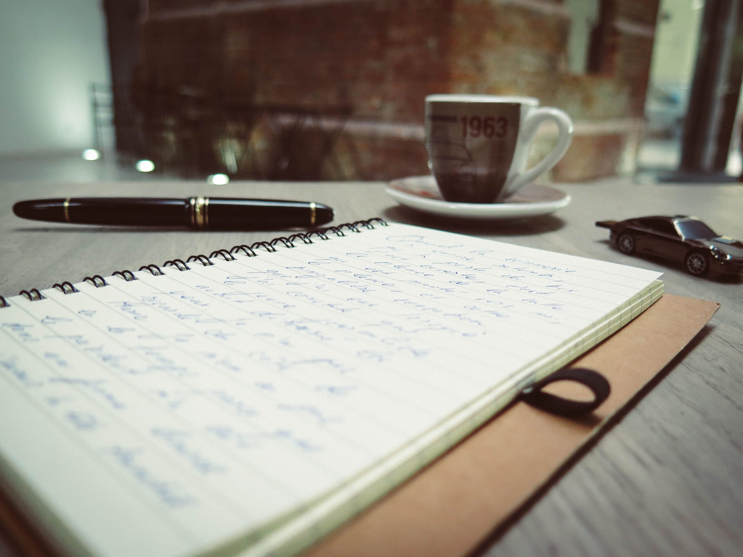 A warm, inviting workspace featuring coffee, handwritten notes, and a pen on the desk.