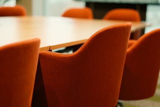 Close-up view of modern orange chairs around a conference table in an office setting.